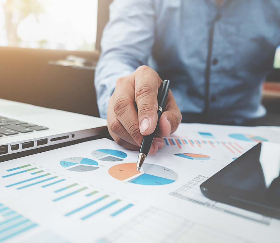A hand holding a pen pointed at graphs on paper.