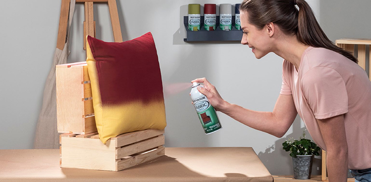 Woman bent over spray painting pillow red.